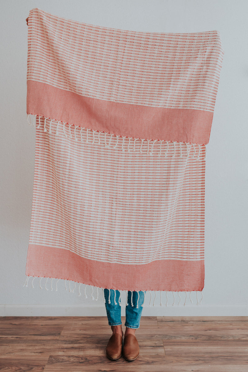 Person holding Bon Ton Studio Mila Turkish Towel in Poppy color in front of wall
